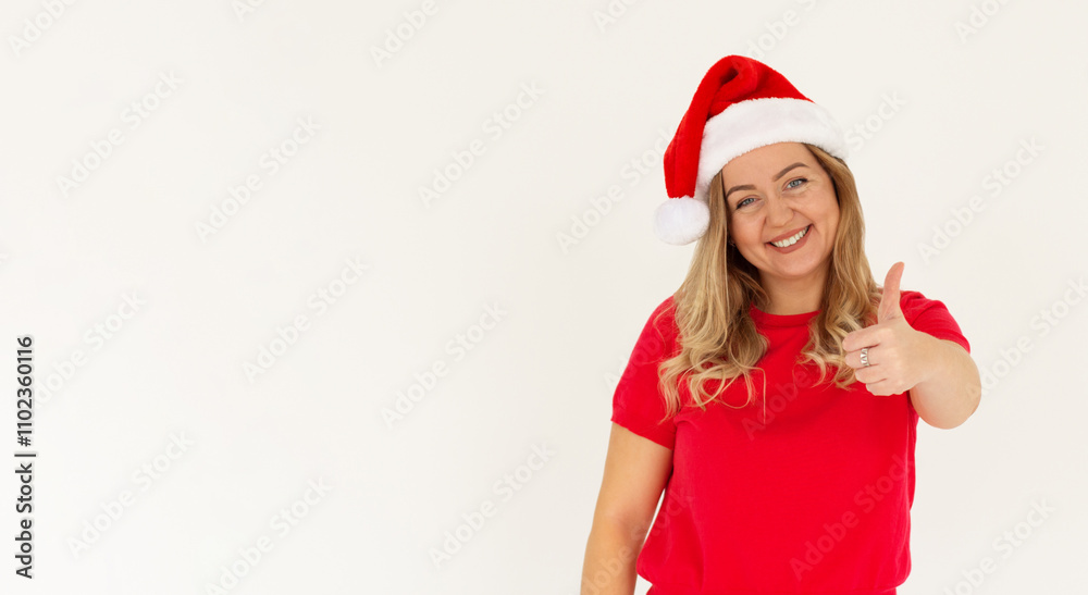 Young funny european woman in red t-shirt and christmas hat showing thumb up and smiling. Happy New Year and Merry Christmas concept Young funny european woman in red t-shirt and christmas hat showing thumb up and smiling. Happy New Year and Merry Christmas concept