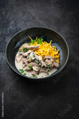 Traditional Swiss Zürcher geschnetzeltes from veal with mushrooms spaetzle in cream sauce served as close-up in a design bowl photo