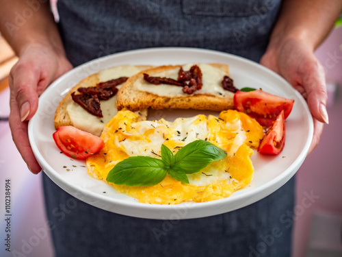 Woman holding plate with continental breakfast - scrambled eggs, bruschetta and fresh vegetables photo