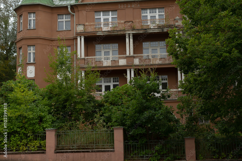 A large brick building featuring a distinctive green roof is beautifully surrounded by lush trees and vibrant bushes in the area A large brick building featuring a distinctive green roof is beautifully surrounded by lush trees and vibrant bushes in the area