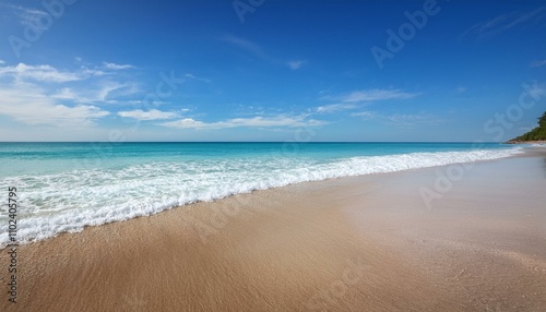 Serene beach scene with gentle waves lapping a sandy shore under a bright blue sky.
