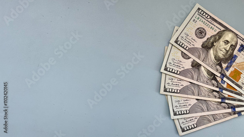 Fan of 100 US dollar bills on a blue background, offering abundant copy space. Ideal for financial advertisements, banking services, or wealth-related content.