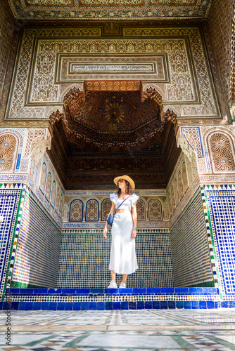 Young Dark Haired Woman in Hat White Shirt and Skirt Posing in the Courtyard of Bahia Palace Marrakech