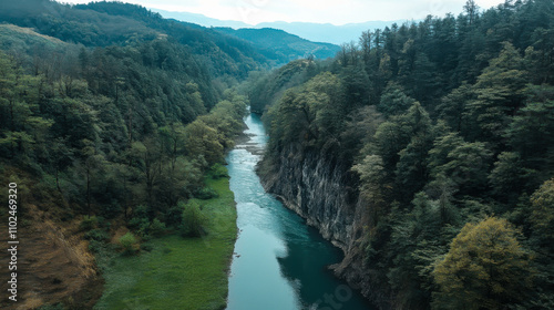 Aerial view of a serene river winding through lush green mountains on a sunny day in a remote wilderness area