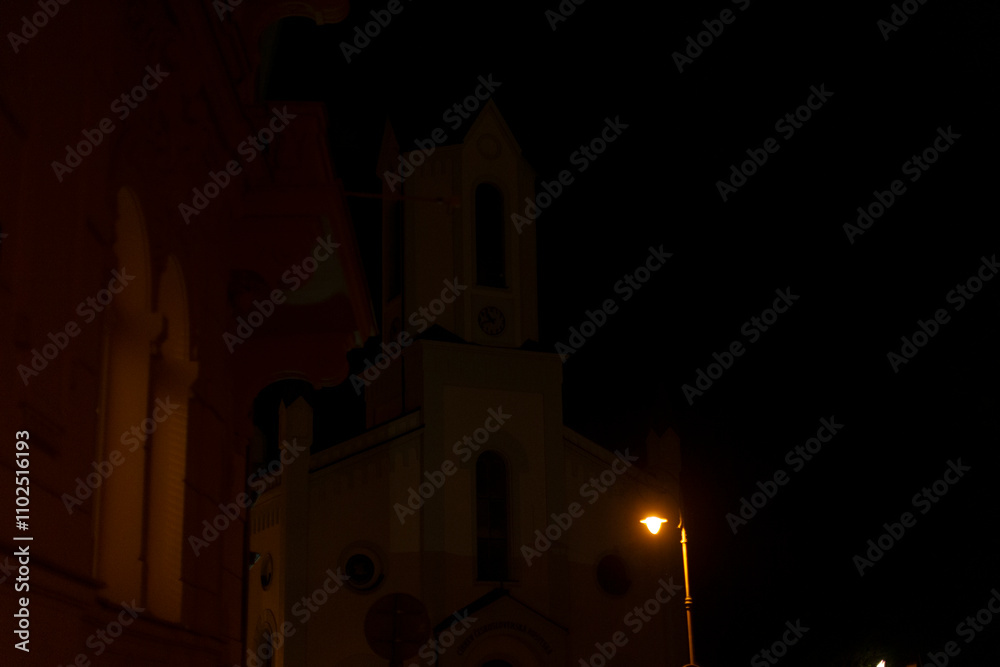 The majestic church stands beautifully illuminated by a glowing streetlight against the dark night sky The majestic church stands beautifully illuminated by a glowing streetlight against the dark night sky