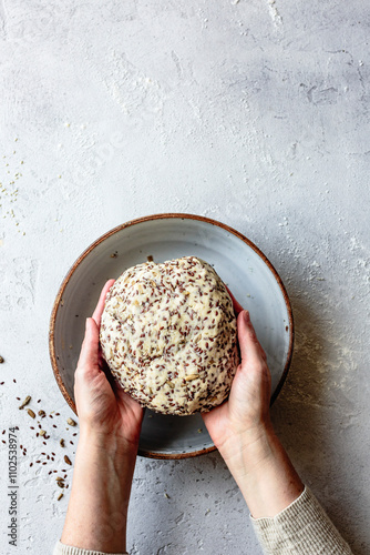 A person holding a round ball of dough with seeds, placed in a ceramic bowl on a textured surface. photo