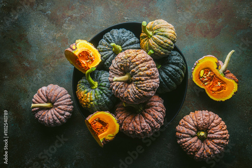 Variety of green and orange heirloom pumpkins, some cut open exposing orange flesh, arranged in black bowl and on custom teal and copper background photo