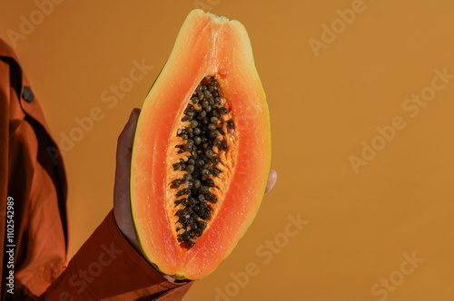 fresh, ripe papaya sliced ​​open in woman's hands, on orange background, harsh sunlight