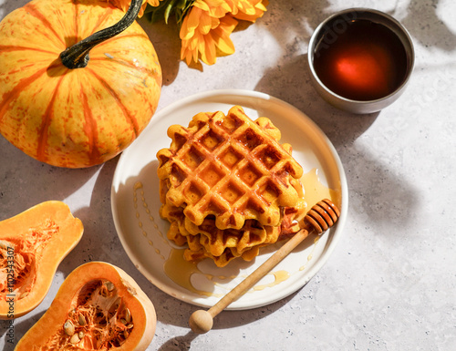 pumpkin waffles drizzled with honey on a white plate, surrounded by autumn-themed decorations including a whole pumpkin photo