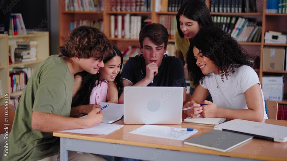 Diverse group of high school young students working together using and looking at laptop in library. Happy Generation Z classmates multiracial friends studying sitting with computer on class project