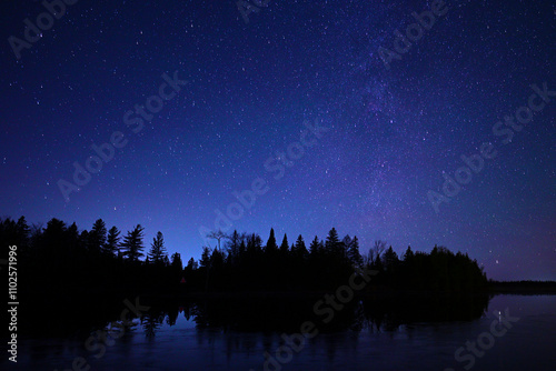 A night scene of a star filled sky and a faint glow of the Milky Wway over a calm fresh water lake photo