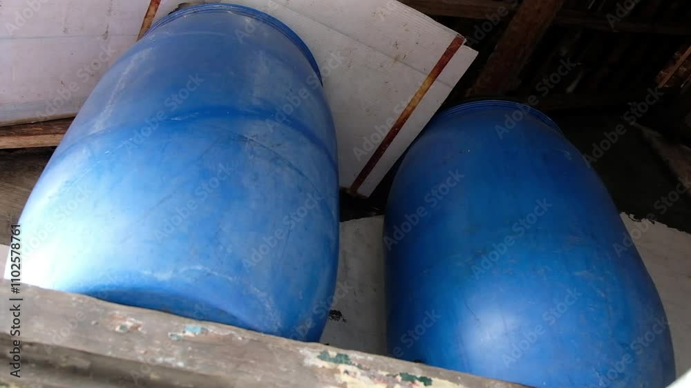 Two weathered blue plastic barrels rest on old wooden planks within a rustic building. Ideal for industrial, rural, storage, or texture themes. Two weathered blue plastic barrels rest on old wooden planks within a rustic building. Ideal for industrial, rural, storage, or texture themes.