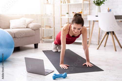 Personal trainer giving online workout class via laptop at home, doing plank or push up exercise