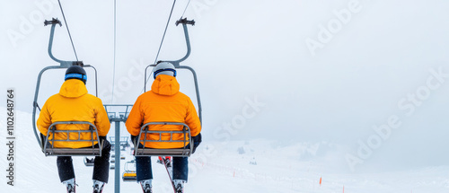 Two skiers on a chairlift ascend through a snowy landscape, wearing bright yellow jackets against a foggy, winter backdrop. photo