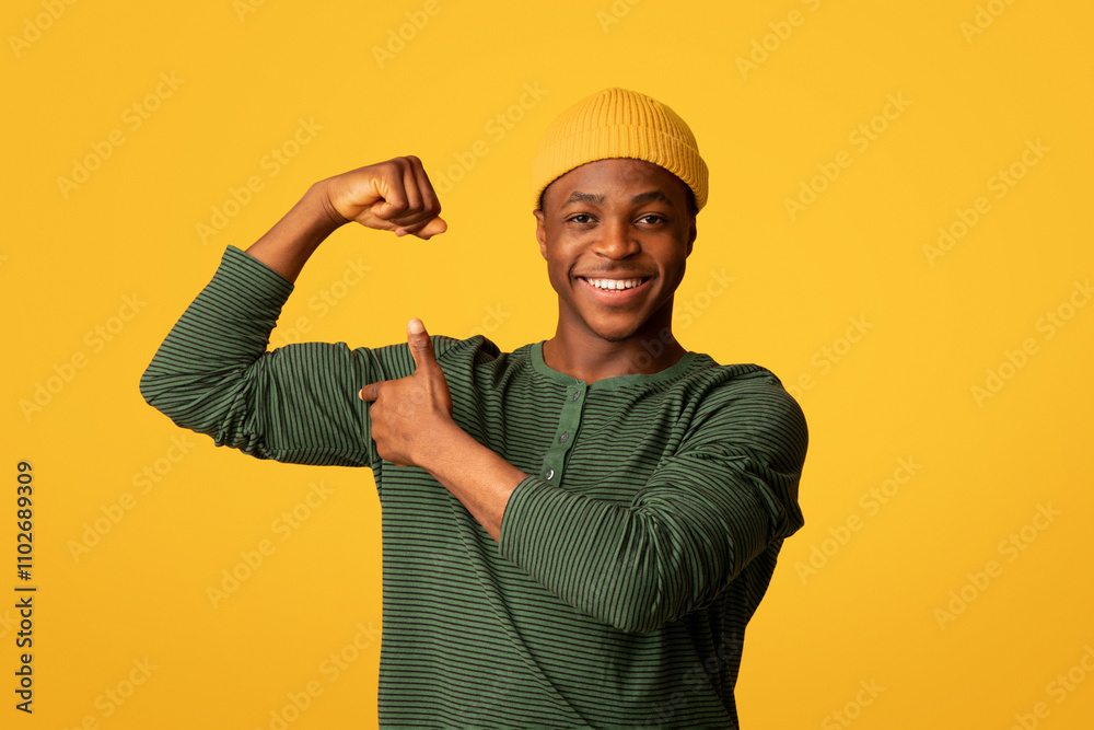 Cheerful Young Black Man Pumping Fist And Pointing At His Biceps, Positive African Millennial Hipster Guy Showing Muscles, Demonstrating Power And Strength While Posing Over Yellow Studio Background Cheerful Young Black Man Pumping Fist And Pointing At His Biceps, Positive African Millennial Hipster Guy Showing Muscles, Demonstrating Power And Strength While Posing Over Yellow Studio Background