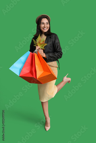 Young woman with shopping bags and autumn leaves on green background