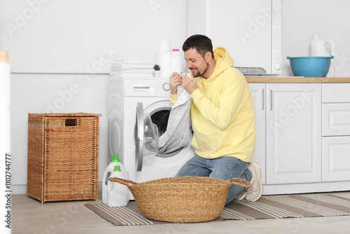 Quadro em tela Young man smelling clean laundry from washing machine at home