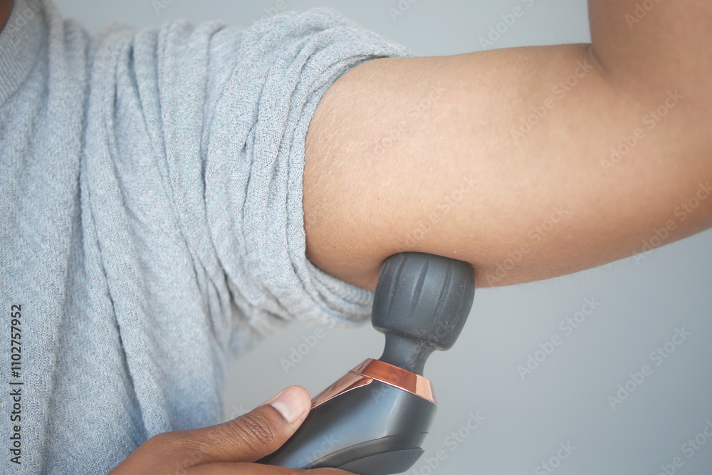 Fototapeta premium Individual Applying a Massage Gun to Their Arm for Effective Muscle Relaxation and Relief