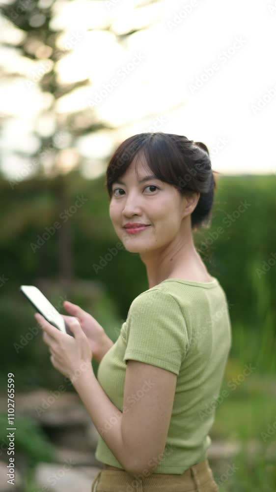 Vertical video of Smiling Woman Green Shirt Using Smartphone Outdoors Vertical video of Smiling Woman Green Shirt Using Smartphone Outdoors