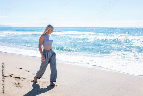 Obraz na płótnie Thoughtful young girl walking along the seashore. Pretty blonde in gray casual clothes. w salonie
