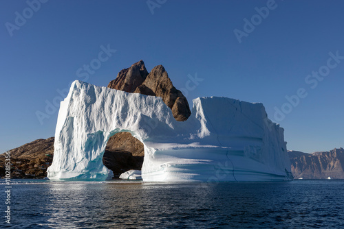 Huge Iceberg with a an arch in front of Uummannaq island, Greenland, view from the ocean photo