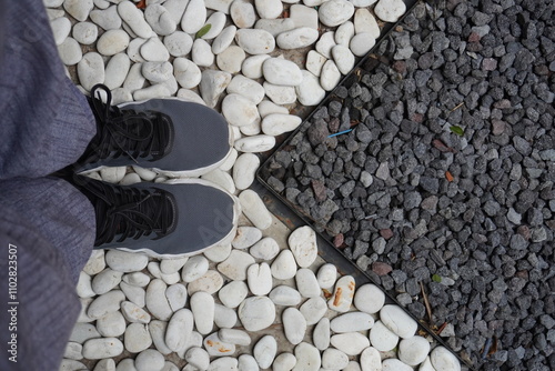 A person wearing trousers and shoes standing on white gravel with a line separating the black gravel photo