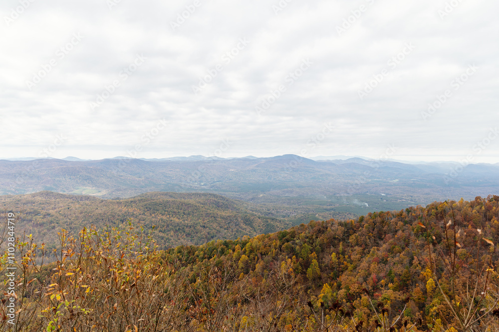 Beautiful autumn landscape with rocks, mountains and forest with yellow and red leaves on trees. Road among mountains in North Carolina, USA.
