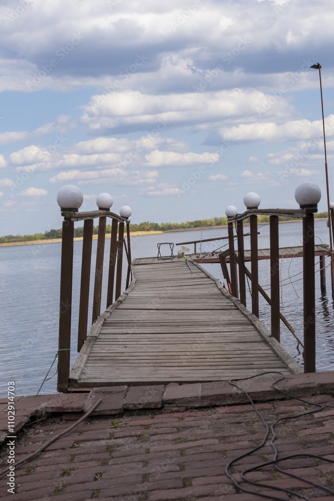 Obraz premium Wooden pier with wooden fencing on the bank of the Vorskla River. Landscape with a fishing pier on the river