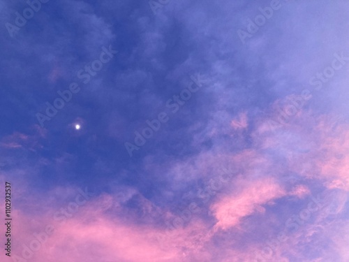 the winter vanilla sky is a mix of blue and pink with floating white clouds and a soft moon is slowly rising