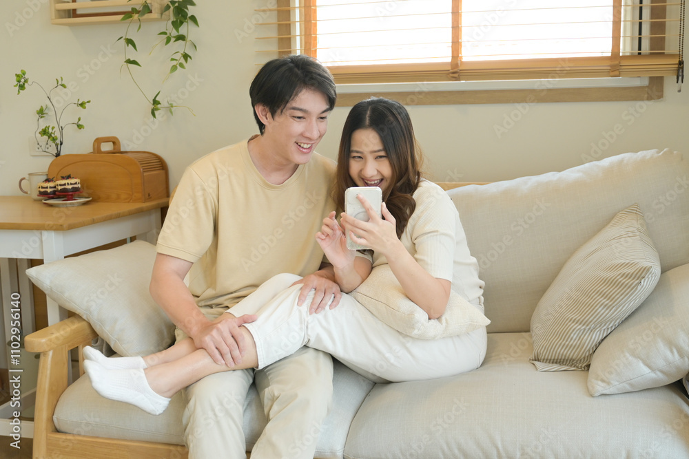 A man and woman are sitting on a couch, both looking at their cell phones. A man and woman are sitting on a couch, both looking at their cell phones.