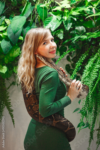 Pretty young woman holding a snake at a reptile encounter, symbolizing an exciting and educational animal interaction, against floral wall
