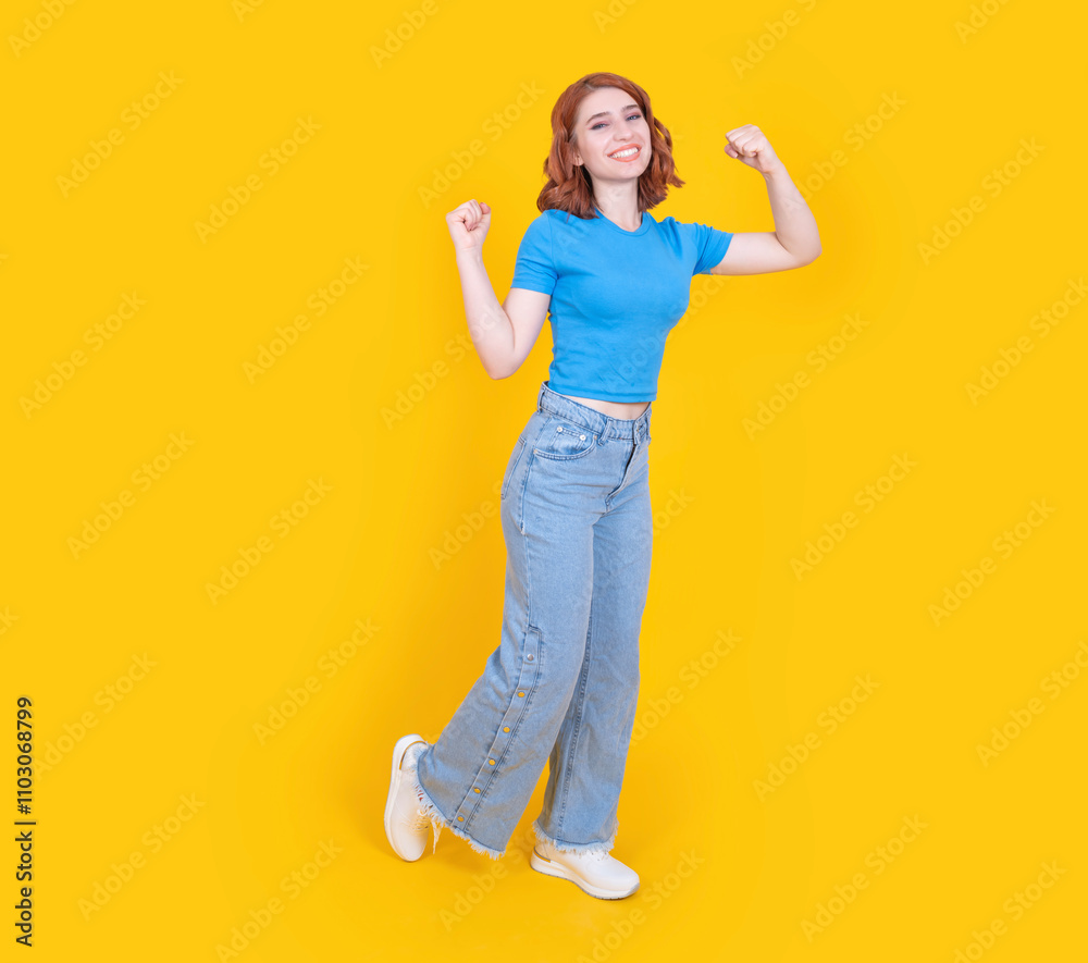 Powerful woman, full body view confident full body 20s powerful woman posing isolated over yellow studio background, copy space. Showing winner pose, clenched fists. Wear casual jean and t shirt. Powerful woman, full body view confident full body 20s powerful woman posing isolated over yellow studio background, copy space. Showing winner pose, clenched fists. Wear casual jean and t shirt.