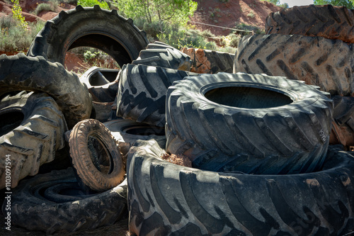 A pile of large worn tractor tires stacked in the field
