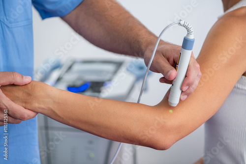 A physical therapist uses laser therapy on a patients elbow to alleviate pain and accelerate healing. The laser treatment targets soft tissues to reduce inflammation and promote recovery photo