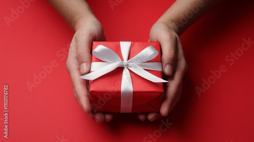 A photo of a pair of hands gently holding a red gift box with a white ribbon against a vibrant red background. The gift box is wrapped with red paper and ai generated