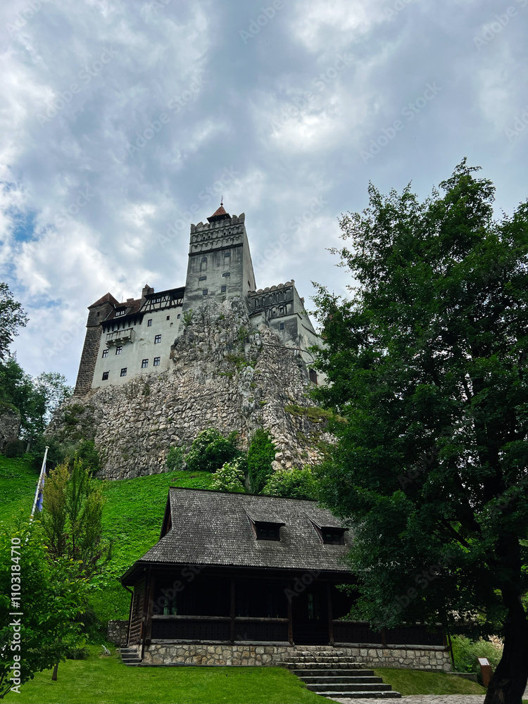 Majestic Bran Castle with lush greenery under a dramatic sky