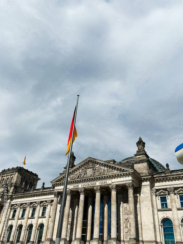 Obraz premium Historical landmark Reichstag building with German flag and cloudy sky