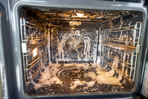 Obraz na płótnie A close-up of a hand in a black glove spraying cleaning solution inside a dirty oven. The foam cleaner is applied to remove grease and grime, ensuring a spotless and hygienic appliance w salonie