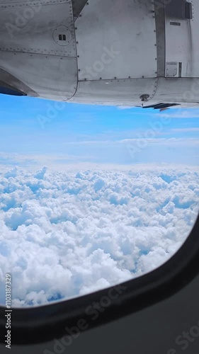 Aerial view of a blue sky with fluffy white clouds through an airplane window, flying above the clouds. Travel concept. freedom, adventure, wanderlust, relaxation. 4K video vertical