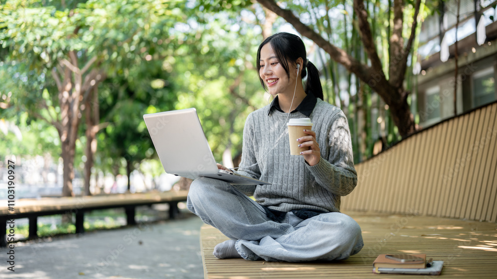 A woman enjoys a hot drink while working remotely outdoors, sits on a park bench with her laptop. A woman enjoys a hot drink while working remotely outdoors, sits on a park bench with her laptop.