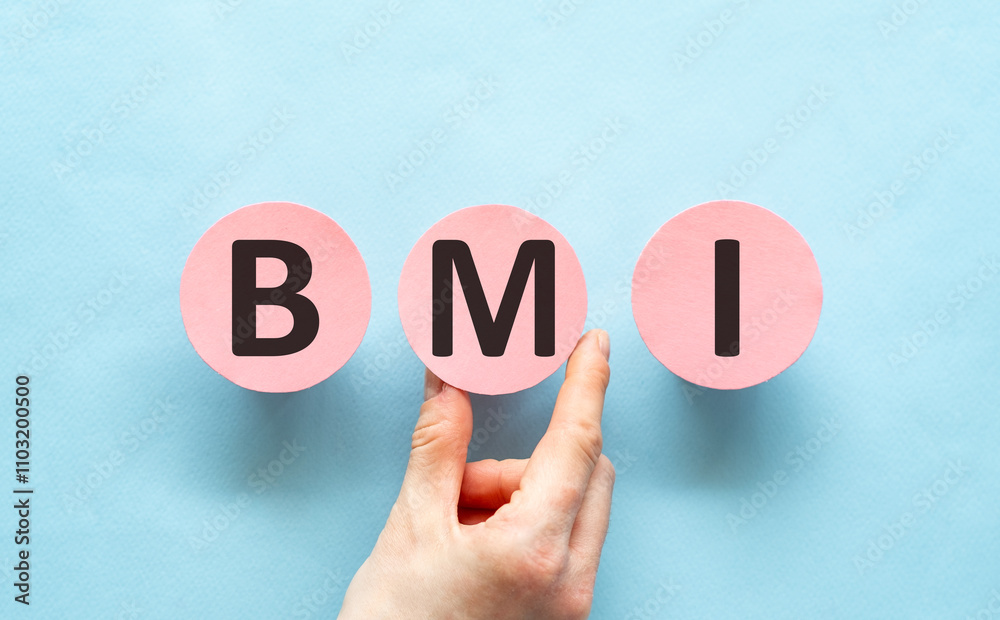 Pink circles with letters forming the acronym BMI held up by a hand against a blue background Pink circles with letters forming the acronym BMI held up by a hand against a blue background