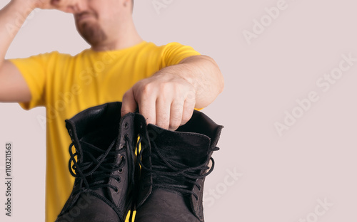 Man holding smelly boots with unpleasant odor, pinching nose photo