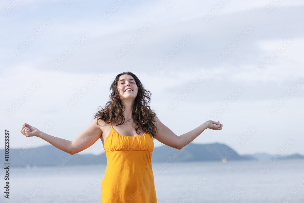 Happy Woman in Orange Dress Standing with Arms Open on a Sunny Beach, Smiling and Enjoying Freedom, Embracing Nature, Peace, and Joy with Scenic Ocean and Mountain Background Happy Woman in Orange Dress Standing with Arms Open on a Sunny Beach, Smiling and Enjoying Freedom, Embracing Nature, Peace, and Joy with Scenic Ocean and Mountain Background
