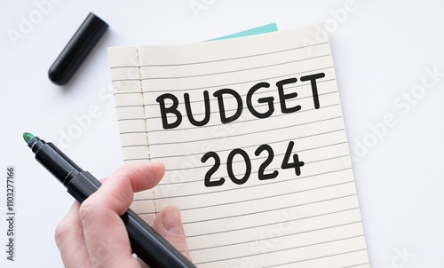 Black marker in hand pointing at open notebook with BUDGET 2024 text on white table