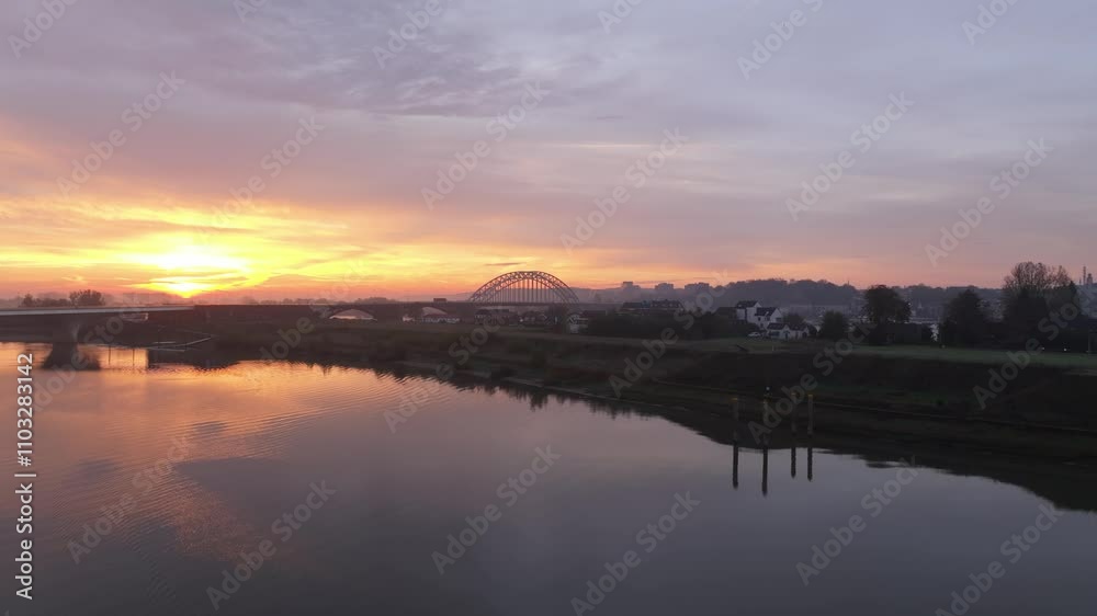 Aerial view of sunrise over the Waal River with the Waalbrug bridge and Stevenskerk church reflecting in the water, Nijmegen, Gelderland, The Netherlands. Aerial view of sunrise over the Waal River with the Waalbrug bridge and Stevenskerk church reflecting in the water, Nijmegen, Gelderland, The Netherlands.
