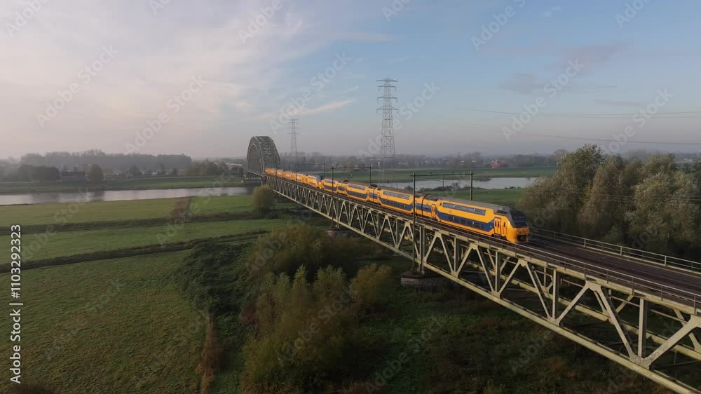 Aerial view of a scenic sunrise over the Rijn River with a railway bridge, fields, and reflections, Oosterbeek, The Netherlands. Aerial view of a scenic sunrise over the Rijn River with a railway bridge, fields, and reflections, Oosterbeek, The Netherlands.