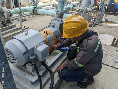 A technician is inspecting an industrial pump, wearing safety gear and checking the equipment.
