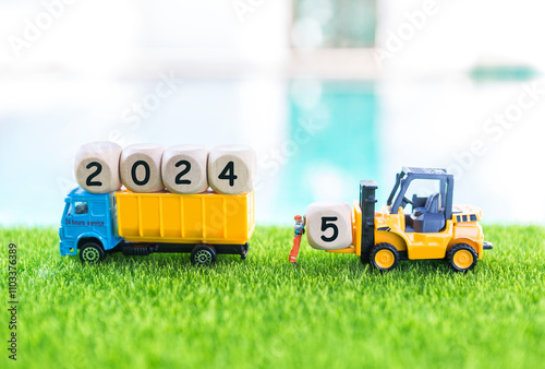 Good bye 2024 welcome 2025, wooden cube on forklift truck and service truck on green grass over blurred background photo