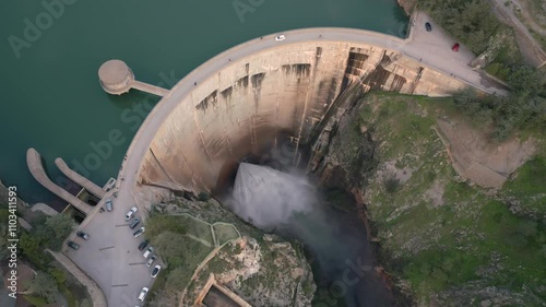 Vault dam inside a mountain canyon discharging water into the river. Ascending aerial view. Quentar Dam. Spain. photo