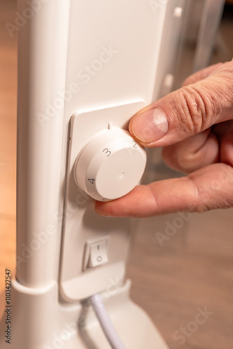 The man's hand regulates the temperature of the electric heater. Electric energy.